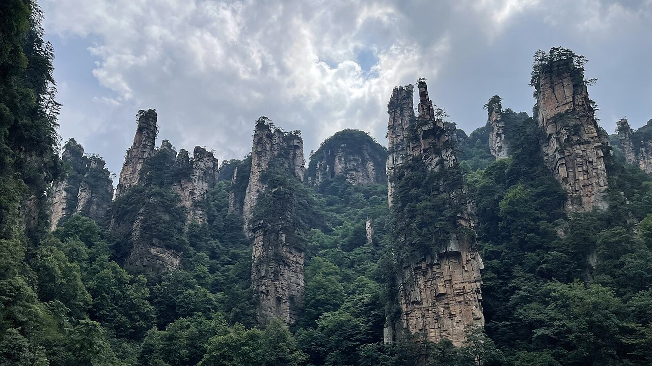 Tall sandstone pillars covered with trees beneath a cloudy sky in Wulingyuan, Zhangjiajie